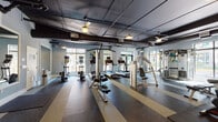 This fitness center offers a comprehensive workout environment designed to accommodate a wide range of exercise needs. The space features an open, single-floor layout with generously high ceilings that lend an airy, spacious feel. Exposed ductwork and piping along the dark ceiling give the facility a distinctive industrial aesthetic, complemented by soft blue-gray walls and pendant-style lighting fixtures paired with ceiling fans for climate comfort.

The flooring consists of durable rubber gym flooring in a bold striped pattern of dark and light tones, providing both safety and visual interest throughout the space. Large windows along multiple walls invite abundant natural light and offer views of the surrounding outdoor greenery, creating an energizing atmosphere for workouts.

The cardio section is well-stocked with multiple treadmills and elliptical machines, while the strength-training area includes cable machines, a multi-functional cable/pulley system, rowing machine, and a variety of benches. Large wall-mounted mirrors are strategically placed to maximize the sense of space and allow users to monitor their form. Double glass doors provide convenient access to the exterior, further reinforcing the connection between indoor and outdoor environments. Colorful abstract artwork adds a vibrant touch to the functional space.