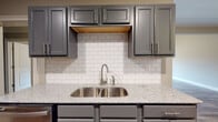 This single-floor home offers a thoughtfully designed layout with a cohesive blend of modern finishes and functional living spaces. The galley-style kitchen is a standout feature, showcasing slate-gray raised-panel cabinetry, light gray granite countertops, a white subway tile backsplash, and stainless steel appliances including a range, microwave, and refrigerator. Warm wood-look vinyl plank flooring runs throughout the kitchen and main living areas, adding a sense of continuity and warmth.

The living room impresses with soaring vaulted ceilings, a ceiling fan, and French doors that invite natural light and provide outdoor access. A built-in niche adds architectural interest to the space. The open sightlines connect the living area to the kitchen, creating a welcoming flow throughout the main living zone.

Bedrooms are carpeted for comfort and feature ceiling fans and windows that bring in natural light with views of the surrounding greenery. The bathrooms maintain the home's consistent design language, with gray cabinetry, granite vanity tops, and brushed nickel fixtures. The primary bathroom offers both a soaking tub with tile surround and a separate glass-enclosed shower, providing a relaxing, spa-like retreat.