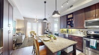 This single-floor residence offers a thoughtfully designed open-concept layout that seamlessly connects the kitchen, dining, and living areas. The kitchen is a standout feature, showcasing rich dark wood cabinetry, granite countertops, stainless steel appliances, a subway tile backsplash with under-cabinet lighting, and a large granite-topped island that doubles as a dining space with seating for multiple guests. Industrial-style pendant lights hang above the island, adding a modern touch. Adjacent to the kitchen, a built-in desk area with matching dark wood cabinetry provides a dedicated workspace.

The living room is bathed in natural light from large floor-to-ceiling windows and sliding glass doors, offering outdoor views and an open, airy feel. A contemporary chandelier anchors the space, which flows comfortably for both lounging and entertaining.

The bedroom is a serene retreat, featuring plush carpet, natural light from large windows, and ample space. A walk-in closet with built-in shelving provides generous storage, and an in-unit stacked washer/dryer adds everyday convenience.

The bathroom is well-appointed with wood-look tile flooring, a granite-topped dark wood vanity, and a full tub-shower combination with floor-to-ceiling tile surround. Throughout the residence, wood-style flooring, neutral tones, and cohesive finishes create a polished, contemporary ambiance.