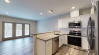 Located at 22 Washington Ave in Sandy Hook, CT, this single-floor space presents a clean, contemporary design highlighted by an open-concept layout that seamlessly connects the kitchen and living area. The kitchen is well-appointed with white shaker-style cabinetry, light quartz countertops, a subway tile backsplash, and a full suite of stainless steel appliances, including a French door refrigerator, electric range, microwave, and dishwasher. A peninsula with a built-in sink and additional counter space serves as a natural divider between the kitchen and the main living area, offering both functionality and a social focal point.

The living area is generously proportioned, bathed in natural light from a set of French doors that open to an outdoor deck with views of surrounding trees. Wood-look plank flooring runs throughout the main areas, adding warmth and continuity to the space. Recessed lighting and a track light fixture provide layered illumination throughout.

The bedroom is a calm, neutral-toned room with a window that draws in natural light. The bathroom features a dark espresso vanity with a white countertop, a large mirror, and light-toned tile flooring. Additional utility areas, including a closet and electrical panel nook, contribute to the overall practicality of this well-designed space.