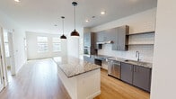 This contemporary 1010 square foot apartment offers a harmonious blend of functionality and style. The open-concept layout seamlessly integrates the kitchen, living, and dining areas, creating an expansive feel. The kitchen boasts sleek gray cabinetry, stainless steel appliances, and a substantial island with granite countertops, perfect for casual dining or entertaining.

Natural light floods the space through large windows, complementing the warm wood-look flooring throughout. The primary bedroom, measuring 180 square feet, provides ample space and includes a ceiling fan for comfort. Both bathrooms feature modern finishes, with one showcasing a tiled shower and generous vanity space.

In-unit laundry adds convenience, while built-in closets offer plentiful storage. The apartment's neutral color palette and clean lines create a canvas for personal style. Large windows in the bedrooms and living area not only brighten the space but also offer views of the surrounding area. This well-designed apartment combines comfort and contemporary living in a compact yet efficient layout.