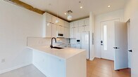 Located at 2722 N 7th St in Phoenix, AZ, this two-story home offers a thoughtfully designed layout across two floors. The main level features an open-concept living, dining, and kitchen area beneath dramatic double-height ceilings that flood the space with natural light. Large floor-to-ceiling sliding glass doors lead to a patio, framing outdoor views and enhancing the airy, expansive feel. Exposed concrete beams add an industrial character that contrasts beautifully with the clean white palette throughout. The kitchen is outfitted with white cabinetry extending to the ceiling, a white tile backsplash, white appliances, pendant lighting, and a central island with a matte black faucet — a striking design detail echoed across both bathrooms. Light-toned large-format tile flooring runs through the main level, while the upper floor transitions to plush carpet. The spacious primary bedroom is located upstairs, featuring a ceiling fan and direct access to a private bathroom with a fully tiled walk-in shower, a natural light window, and matte black fixtures. A second full bathroom on the main level features a sleek white vanity with an undermount sink and large mirror. A dedicated laundry area and a closet round out the functional layout of this modern Phoenix home.