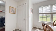 Located at 150 Wexford Pl in Webster, NY, this single-floor residence offers a practical and comfortable layout encompassing one bedroom, one bathroom, and a generous open-plan living area. The entryway welcomes with light-toned luxury vinyl plank flooring and a bright, airy atmosphere thanks to natural light streaming through blinds-fitted windows with pleasant outdoor green views.

The combined living, dining, and kitchen area forms the heart of the home. The living room features a cozy layout with a fireplace console, large windows with access to an exterior door, and easy flow into the dining area, which is illuminated by a classic chandelier and overlooks the greenery outside. The galley-style kitchen offers warm wood cabinetry lining both walls, ample counter space, and full appliance suite including a dishwasher and range.

The spacious bedroom is carpeted for comfort and includes a large walk-in closet with extensive built-in shelving and hanging storage. The full bathroom features a wood-toned vanity, wide mirror with overhead lighting, and durable vinyl plank flooring. A dedicated in-unit laundry room houses a full-size washer and dryer with additional shelving, completing the home's practical amenities.