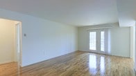 This single-floor space offers a clean, open layout defined by its warm, polished hardwood floors that reflect natural light throughout the room. The floors display a classic honey-toned wood grain, adding character and warmth to the otherwise neutral interior. Crisp white walls provide a blank canvas, making the space highly versatile and well-suited to a variety of design preferences.

A standout feature is the set of elegant French doors positioned along the exterior wall, framed in white and fitted with divided-light glass panes. These doors serve as both a functional entry point and a significant source of natural light, brightening the interior and offering a visual connection to the outdoors. The smooth, white ceiling complements the light walls, contributing to an airy and uncluttered atmosphere.

The open floor plan allows for flexible furniture arrangements, and the absence of interior partitions maximizes the sense of spaciousness. Overall, the space presents a bright, move-in-ready environment with timeless finishes that provide a strong foundation for personalization.