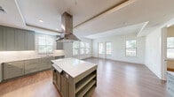 Located in Austin, TX, this well-appointed single-story residence offers three bedrooms and three bathrooms within a thoughtfully designed floor plan. The open-concept kitchen and living area serves as the heart of the home, showcasing sage-green cabinetry, a large center island with a white quartz countertop, a stainless steel range hood, and full suite of stainless steel appliances, including a French door refrigerator and double wall oven. Warm hardwood-style flooring flows throughout the main living areas, complementing the clean, neutral palette. The spacious living room is bathed in natural light from multiple windows and a glass-panel door that opens to the outdoors. Each bedroom is bright and well-sized, with large windows offering garden views and ceiling fans for comfort. The primary bedroom includes a dedicated walk-in closet with dual hanging rods and shelving. The bathrooms are elegantly finished with marble-look tile flooring, subway tile tub surrounds in a herringbone pattern, dark cabinetry, and granite-topped vanities. A hallway with built-in cubbies and hooks provides convenient storage near the entry. Two closets add further storage versatility throughout this clean, modern residence.