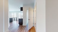 This well-appointed single-floor unit presents a clean, contemporary design throughout. The open-concept layout connects the kitchen and living areas seamlessly, with warm hardwood-style flooring running throughout the space, creating a cohesive and inviting atmosphere.

The kitchen is a standout feature, equipped with full stainless steel appliances including a French door refrigerator, electric range, built-in microwave, and dishwasher. Dark espresso cabinetry paired with a white subway tile backsplash and light countertops provides a striking contrast, while a peninsula with open shelving offers both additional prep space and casual seating potential.

The bedrooms are generously sized and bathed in natural light, courtesy of multiple large windows fitted with horizontal blinds that frame pleasant outdoor views of surrounding greenery and streetscapes. Each room benefits from closet storage and the same warm flooring found throughout.

The bathroom is finished in a modern style, featuring large-format light stone-look tile flooring, a full soaking tub with white tile surround, a spacious vanity with dark wood cabinetry and white countertop, and a well-lit mirror. A secondary bathroom showcases the same tub and tile aesthetic in a crisp, all-white finish.

A welcoming hallway connects the various rooms, maintaining a clean, open flow throughout this thoughtfully designed space.