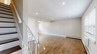 This three-floor home offers a thoughtfully designed layout with consistent, quality finishes throughout. The main level welcomes you with gleaming, polished hardwood floors, neutral grey walls, and recessed lighting that create a bright and open living area. An ornate white wrought-iron staircase adds a distinctive architectural touch. The kitchen has been updated with rich dark wood cabinetry, white quartz countertops, a tile backsplash, stainless steel appliances, and light wood-look tile flooring, offering both style and functionality. The upper level features generously sized bedrooms, each with polished hardwood floors, ample natural light from windows with blinds, and notable built-in storage including shelving units and closets with sliding or hinged panel doors. The bathroom is finished with floor-to-ceiling large-format marble-look tile surrounding the soaking tub, paired with brushed gold hardware for an elevated aesthetic. The basement level provides substantial utility space, housing a full-size front-loading washer and dryer, along with an additional open room featuring painted concrete block walls and a small window — well-suited for storage or flexible use. Baseboard heating is present throughout the home.