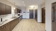 This well-appointed 1-bedroom, 1-bathroom unit is thoughtfully designed with a modern aesthetic and functional layout across a single floor. The open-concept living area features light wood-look flooring, a ceiling fan, and a built-in electric fireplace with a small ledge, creating a warm and inviting focal point. Soft wall sconces add ambient lighting to the living space, which flows seamlessly toward the kitchen.

The kitchen is equipped with stainless steel appliances, including a full-size refrigerator, stove, microwave, and dishwasher. Rich dark wood cabinetry pairs with light countertops and a classic white subway tile backseat accented with a decorative mosaic tile strip. A double stainless steel sink sits beneath a pendant light, and track lighting overhead ensures the workspace is well lit throughout.

A dedicated entryway provides convenient access, with dark-stained six-panel doors adding a refined touch throughout the unit. The bedroom area connects to a versatile space that includes in-unit stacked washer and dryer, a closet with open rod storage, and a built-in countertop surface. The bathroom features tile walls and a clean, functional design. Light wood-look flooring extends through most of the unit, while plush carpet adds comfort in select areas.