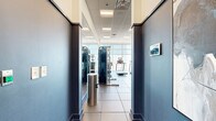 Located at 3242 Peachtree Rd NE in Atlanta's Buckhead neighborhood, this fitness center offers a comprehensive, well-appointed exercise space designed for a full range of workout routines. The room features large, floor-to-ceiling windows along one wall that flood the space with abundant natural light and frame striking panoramic views of the Atlanta skyline, creating an energizing atmosphere for workouts.

The exercise room is finished with large-format tile flooring in a neutral gray tone, complemented by two-tone walls in crisp white and bold blue — giving the space a clean, modern aesthetic. A drop ceiling with recessed panel lighting ensures consistent illumination throughout.

Cardio equipment is prominently featured, including multiple treadmills, an elliptical trainer, and a stair climber, all positioned to take advantage of the city views. A dedicated spin bike with a media screen provides an additional cardio option. For strength training, the space is outfitted with a dual cable machine, a multi-functional rack system, a full set of kettlebells, and an adjustable weight bench. Full-length mirrors along one wall expand the sense of space and allow for proper form checks during exercise. Wall-mounted flat-screen TVs add entertainment convenience. The fitness center is accessible via a secured entry and is thoughtfully organized to maximize usability within its compact footprint.