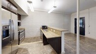 Located at 9380 Quadrangle St, Unit 102 in Lorton, VA, this one-bedroom, one-bathroom residence offers a thoughtfully designed single-floor layout with distinctive architectural character. Exposed painted white brick walls are a defining feature throughout, lending an industrial yet clean aesthetic to the living spaces.

The kitchen serves as a central focal point, equipped with stainless steel appliances including a refrigerator with ice maker and a range, rich dark-wood cabinetry, and a generous granite-topped peninsula with an undermount sink — ideal for both meal preparation and casual dining. Pendant and fluorescent lighting illuminate the space effectively, complementing the stone-tile flooring.

The bedroom is a comfortable, carpeted retreat featuring the same signature white brick walls and black-framed windows that allow natural light to filter in. A closet with louvered doors provides practical storage, and an open doorway connects seamlessly back to the main living area.

The bathroom is designed with accessibility in mind, featuring multiple ADA-compliant grab bars, a walk-in tub/shower combination, a dark-wood vanity with granite countertop, and matching stone-tile flooring that ties the space together. Overall, the unit presents a cohesive blend of industrial charm and functional, accessible design.