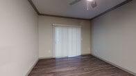 Located at 2811 La Frontera Blvd in Round Rock, Texas, this single-floor residence offers a well-appointed layout with consistent, modern finishes throughout. The living area is highlighted by rich wood-look flooring, decorative crown molding, and a ceiling fan with light fixture, creating a comfortable and polished atmosphere. A sliding glass door fitted with vertical blinds allows natural light to fill the space while providing access to the outdoors. The kitchen is designed in a galley-style configuration, featuring dark cabinetry, stainless steel appliances including a refrigerator, microwave, and range, as well as light countertops and matching wood-look flooring. A pass-through door leads to an adjacent utility or storage area, adding practical functionality. The bedroom offers plush carpeting, a ceiling fan, and a window with horizontal blinds that brings in natural light and views of the surrounding greenery. A second room with wood-look flooring and crown molding provides flexible use as an additional bedroom or living space. The bathroom is clean and functional, featuring a full tub and shower combination with white tile surround, brushed nickel fixtures, and coordinating wood-look flooring. The overall aesthetic is neutral and contemporary, with warm tones creating a cohesive and inviting environment throughout.