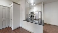 This 610-square-foot, two-bedroom, one-bathroom apartment at 4699 Kittredge Street in Denver, Colorado offers a functional and modern single-floor layout. The open-concept kitchen and living area serves as the heart of the unit, featuring rich dark hardwood-style flooring, white shaker cabinetry, dark granite countertops, stainless steel appliances including a refrigerator, range, microwave, and dishwasher, and a peninsula with a dual-basin sink. The living room extends from the kitchen and is bathed in natural light through double French doors that open to a private balcony. Both bedrooms are carpeted and feature neutral white walls; the primary bedroom spans 140 square feet, while the second bedroom includes a window with outdoor views and a ceiling light fixture. The bathroom is well-appointed with dark granite countertops, white cabinetry, a framed mirror, hardwood-style flooring, and a tub/shower combo surrounded by classic gray subway tile. A dedicated laundry room houses a full-size side-by-side washer and dryer. A closet provides additional storage. The unit's clean, contemporary aesthetic is consistent throughout, with crisp white walls and modern hardware accenting every room.
