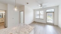 This thoughtfully designed 2-bedroom, 1-bathroom residence in Chester, VA offers a clean, modern aesthetic throughout. The open-concept kitchen is a standout, featuring granite countertops, white shaker cabinetry, a subway tile backsplash, stainless steel appliances, and a large island with pendant lighting. Light wood-style flooring flows through the main living areas, while the bedrooms offer plush carpeting and natural light from wide windows. A stacked washer and dryer is conveniently integrated into the unit. The bathroom includes a granite vanity with a wide mirror and built-in shelving. The living area is bright with a ceiling fan and outdoor views.