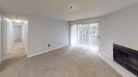 Located at 11328 SE Kent Kangley Rd in Kent, Washington, this single-floor residence offers a functional and comfortable layout across several well-defined living spaces. The open-concept living area is anchored by a fireplace and features plush wall-to-wall carpeting, neutral gray walls, and a textured ceiling. A full-width sliding glass door floods the space with natural light and provides access to a private balcony with views of surrounding greenery, complemented by vertical blinds for adjustable light control. The kitchen is thoughtfully designed with warm wood cabinetry, light countertops, a double sink, and black appliances including a range and refrigerator, all set on durable wood-look flooring. A peninsula counter connects the kitchen to the living area, enhancing the open flow of the space. The bedrooms are generously sized, each finished with soft carpeting, neutral tones, and windows fitted with horizontal blinds that invite natural light while maintaining privacy. The primary bedroom includes access to a dedicated bathroom. Throughout the residence, consistent finishes including textured ceilings, clean white trim, and neutral color palettes create a cohesive and move-in-ready environment.