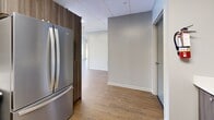 Located at 120 Torresdale Ave in Toronto, this well-appointed party room offers a comfortable and functional setting for private events and social gatherings. The space is thoughtfully laid out across a single floor, providing a generous open-concept footprint that accommodates a variety of event formats.

The main lounge area features warm hardwood-style flooring, a drop tile ceiling with recessed panel lighting, and large windows fitted with roller blinds that allow for natural light while maintaining privacy. The seating arrangement includes a plush sofa, armchairs, and a round coffee table, creating an inviting atmosphere for guests. A wall-mounted flat-screen TV adds a modern entertainment element to the room.

A dedicated flex area, separated by elegant frosted glass French doors, offers additional open space that can be configured as needed. This area also features framed abstract wall art and a console table, lending a refined aesthetic to the room.

The fully equipped kitchen is outfitted with warm wood-toned cabinetry, white countertops, and stainless steel appliances including a full-size refrigerator, electric range, and over-the-range microwave. A utility area with double closets and a separate door provides convenient storage and access. Throughout, the neutral colour palette and consistent flooring create a cohesive, clean, and welcoming environment.