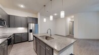 This single-story, 2-bedroom, 2-bathroom residence in Houston, TX offers a well-designed layout with modern finishes throughout. The open-concept kitchen serves as a central highlight, featuring gray shaker-style cabinetry, granite countertops, a subway tile backsplash, stainless steel appliances including a refrigerator, range, and microwave, and a large center island with pendant lighting overhead. Light wood-style flooring extends through the kitchen and living areas, contributing to a clean, contemporary aesthetic.

The living area is bright and open, benefiting from natural light through large windows and a sliding door, and is equipped with a ceiling fan. Both bedrooms are comfortably sized and carpeted, each with windows and ceiling fans. The spacious primary bedroom includes a well-organized walk-in closet with built-in shelving and hanging rods. Both bathrooms are finished with granite-topped vanities, framed mirrors, and tub-shower combinations with tiled surrounds.

The unit also features a private fenced outdoor area with a grassy yard and views of the surrounding landscaped community, including mature palm trees. Two dedicated closets add practical storage throughout.