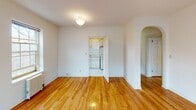 Located at 2427 Third Ave S in Minneapolis, this single-floor unit blends classic architectural charm with functional design. Polished hardwood floors run throughout the living areas, reflecting natural light and adding warmth to each room. A defining architectural feature is the graceful arched doorway connecting the entry hall to the main living space, lending a sense of elegant character to the layout.

The living area is generously proportioned, with large multi-pane windows on multiple walls that invite abundant natural light and offer views of the surrounding neighborhood. A cast-iron radiator provides classic in-unit heating. The open, neutral-toned walls create a clean, versatile backdrop throughout.

A separate kitchen features white cabinetry and appliances, accessible through a standard doorway from the main living room. The bathroom is finished with white tile flooring and tile surround, and includes a full soaking tub with shower, a window for natural ventilation, and a clean, minimal aesthetic consistent with the rest of the unit.

Overall, the space presents a bright, classic ambiance defined by its warm hardwood floors, arched passageways, multi-pane windows, and timeless detailing throughout.
