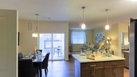 Located at 740 Bridgeport Avenue in Shelton, Connecticut, this single-floor residence offers a thoughtfully designed open-concept layout that seamlessly connects the kitchen, dining, and living areas. The kitchen is anchored by a granite countertop island with rich dark cabinetry below, providing ample prep and storage space. Stylish pendant lighting hangs above, adding a contemporary touch to the space. The kitchen flows naturally into the dining area, which is well-lit and comfortably accommodates a full dining set beneath additional pendant fixtures. Warm hardwood flooring runs throughout, lending a cohesive and inviting feel to the main living area. A sliding glass door in the dining area provides direct access to an outdoor patio, allowing natural light to pour into the space while offering a seamless indoor-outdoor connection. The living room, situated adjacent to the dining area, is bright and airy thanks to large windows dressed with curtains. The neutral wall tones and warm flooring create a welcoming ambiance throughout, making this a comfortable and functional single-level home in the heart of Shelton, CT.