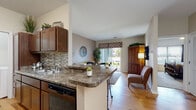 Located at 3604 Spring Villa Cir in Louisville, KY, this single-floor home offers a well-designed, open layout that connects the kitchen, dining, and living areas seamlessly. The kitchen features rich wood cabinetry, granite-style countertops, a mosaic tile backsplash, and black appliances, including a range and dishwasher. A peninsula with bar seating provides additional workspace and a casual dining option. The adjacent living area is bright and welcoming, with hardwood-style flooring and a sliding glass door that opens to a private outdoor patio with outdoor seating and neighborhood views. The dining area accommodates a full-sized table and is accented by a chandelier overhead. Both bedrooms are carpeted and offer natural light through large windows with stylish drapery. The full bathroom includes tile flooring, a soaking tub with shower, and a wood vanity topped with granite-style counters. A dedicated in-unit laundry space with washer and dryer adds everyday convenience. Throughout the home, neutral tones and consistent finishes create a cohesive and comfortable living environment.