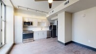This single-floor unit offers a contemporary design with a practical and open layout. The main living area is bright and airy, benefiting from multiple large, black-framed windows that allow abundant natural light to fill the space. A glass door provides direct access to an outdoor balcony, offering open sky views. A ceiling fan overhead adds both function and a modern touch to the living space.

The kitchen is well-appointed and efficiently designed, featuring stainless steel appliances including a range, microwave, dishwasher, and refrigerator. White cabinetry with clean-lined hardware lines the walls, complemented by a white subway tile backsplash, light countertops, and a double stainless steel sink. Track lighting overhead ensures the kitchen is well-lit.

Wood-style plank flooring extends consistently throughout the living and kitchen areas, providing a warm yet modern aesthetic. Dark baseboards offer a sharp contrast against the neutral walls.

The bathroom is clean and straightforward, featuring a full tub-shower combination with white tile surround. Overall, the unit maintains a cohesive, modern aesthetic with neutral tones throughout.
