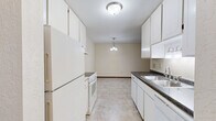 This single-floor residence in Hastings, MN, offers a practical and comfortable layout with two bedrooms, one bathroom, and a combined kitchen and living area. The galley-style kitchen features white cabinetry, dark countertops, tile flooring, and white appliances including a range and refrigerator, with a pendant light fixture illuminating the adjoining dining area. The living room is carpeted and benefits from a large window with vertical blinds that frames a pleasant outdoor view of mature trees, while a wall-mounted air conditioning unit ensures year-round comfort. Both bedrooms are finished with soft carpet and neutral walls. The spacious primary bedroom includes access to a generously sized walk-in closet outfitted with multiple shelving rods and storage shelves, as well as an additional louvered bifold closet. The second bedroom also offers closet access and features a ceiling fan and a window with natural light. The full bathroom is finished with tile flooring, a tub-shower combination with white tile surround accented by diamond details, a vanity with under-cabinet storage, and a toilet. Throughout the residence, warm wood-toned doors and trim provide a consistent, cohesive design element.