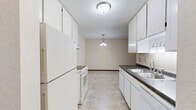 This single-floor residence in Hastings, MN, offers a practical and comfortable layout with two bedrooms, one bathroom, and a combined kitchen and living area. The galley-style kitchen features white cabinetry, dark countertops, tile flooring, and white appliances including a range and refrigerator, with a pendant light fixture illuminating the adjoining dining area. The living room is carpeted and benefits from a large window with vertical blinds that frames a pleasant outdoor view of mature trees, while a wall-mounted air conditioning unit ensures year-round comfort. Both bedrooms are finished with soft carpet and neutral walls. The spacious primary bedroom includes access to a generously sized walk-in closet outfitted with multiple shelving rods and storage shelves, as well as an additional louvered bifold closet. The second bedroom also offers closet access and features a ceiling fan and a window with natural light. The full bathroom is finished with tile flooring, a tub-shower combination with white tile surround accented by diamond details, a vanity with under-cabinet storage, and a toilet. Throughout the residence, warm wood-toned doors and trim provide a consistent, cohesive design element.