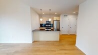 Located at 928 in Madison, WI 53703, this thoughtfully designed 780-square-foot apartment offers 2 bedrooms and 2 bathrooms across a single floor. The open-concept kitchen and living area serves as the heart of the unit, featuring light wood cabinetry, striking black marble-veined countertops, a central island with an integrated sink, stainless steel appliances, and a decorative pendant light. Light hardwood flooring flows throughout the main living spaces, complementing the clean white walls and recessed lighting. A distinctive architectural highlight is the exposed natural wood beam ceiling, adding warmth and character to the space. The bedrooms feature plush carpet flooring, large black-framed windows offering urban views of the Madison skyline and surrounding buildings, and sliding panel closets. The primary bedroom measures 140 square feet. Both bathrooms are finished with bold, dark vertical tile in the wet areas — one with a soaking tub and shower combination, and the other with a walk-in glass shower — paired with dark stone vanity countertops and light wood cabinetry. Natural light is abundant throughout, with multiple large windows framing dynamic city views.
