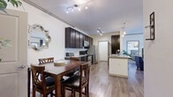 This single-floor residence offers a thoughtfully designed layout that seamlessly connects the main living areas. The kitchen is a standout feature, showcasing rich dark espresso cabinetry extending to the ceiling, granite countertops, a tile backsplash, and a full suite of stainless steel appliances including a range, microwave, and refrigerator. Track lighting illuminates the space, highlighting both the generous counter space and the adjacent peninsula with an undermount sink. The open dining area flows naturally from the kitchen, providing an inviting space anchored by hardwood-style flooring that carries throughout the main living areas. Crown molding adds a refined touch to the dining nook. The living room is warm and relaxed in character, featuring a ceiling fan, soft neutral walls, and wood-look flooring, with access to additional rooms. The bedroom is carpeted and well-lit with multiple windows dressed in striped curtains, and a ceiling fan adds comfort overhead. A generously sized walk-in closet with wire shelving provides ample storage. The bathroom is finished with dark cabinetry, granite countertops, and light wood-look flooring, maintaining the consistent aesthetic found throughout the residence.
