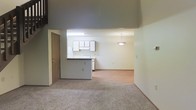 Located at 1237 Watermark Drive in Lancaster, Ohio, this two-story residence offers a functional and open layout across two levels. The main level showcases an open-concept design where the kitchen flows seamlessly into the dining and living areas. The kitchen features white cabinetry, a peninsula with counter seating, and under-cabinet lighting, providing both practicality and a clean aesthetic. A pendant light fixture hangs above the dining area, adding a warm focal point to the space. The living area is finished with neutral carpet, contributing to a comfortable and cohesive feel throughout. The ceiling height on the main level is notably tall, creating an airy, expansive atmosphere that enhances the sense of openness. Light-toned walls throughout the main floor keep the space feeling bright and welcoming. A separate door off the main living area provides additional access or utility. The transition between the carpeted living space and the hard-surface kitchen flooring adds visual distinction between the zones. The second floor offers additional living space, accessible from the main level. Overall, the residence presents a straightforward, well-organized floor plan suited for everyday living.