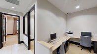 Located at 1 Garden Park Blvd in Cherry Hill, NJ, this polished business center offers a well-appointed single-floor layout designed to support professional productivity. The space is organized around a central hallway connecting a welcoming entrance, dedicated workstation areas, and a standout conference room.

The conference room is the centerpiece of the space, featuring a large dark rectangular table surrounded by ergonomic chairs. Three striking spherical woven pendant lights hang overhead, casting warm ambient light that complements the recessed ceiling fixtures. A wall-mounted display screen and built-in dark wood cabinetry with a service counter add functional elegance. Large windows dressed with floor-length striped drapes invite natural light and offer views of the surrounding greenery.

The individual workstation areas are clean and functional, each equipped with built-in light wood desks, desktop computers, and task chairs. Dark-framed glass partition doors lend a sleek, modern aesthetic throughout, while light-toned tile flooring in the hallway transitions to soft carpet in the workspaces. The neutral white walls and dark wood baseboards create a cohesive, professional environment. Security cameras are discreetly integrated into the ceiling. Overall, the space balances contemporary design with practical functionality.