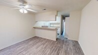 This efficiently designed 490-square-foot, one-bedroom, one-bathroom apartment is laid out on a single floor, offering a functional and cohesive living environment. The combined kitchen and living room serves as the heart of the unit, featuring durable wood-style laminate flooring, neutral cream-toned walls, and ceiling fans with integrated lighting throughout. The living area benefits from a sliding glass door that opens to an outdoor area, allowing natural light to fill the space. A pass-through counter connects the living area to the galley-style kitchen, which is outfitted with white cabinetry, laminate countertops, a stainless steel sink, and white appliances including a range, refrigerator, and overhead ventilation hood. The 150-square-foot primary bedroom provides a comfortable retreat, equipped with a ceiling fan, a large window with vertical blinds, and the same laminate flooring found throughout the unit. A dedicated closet adds practical storage. The full bathroom features a single-sink vanity with a wood-toned cabinet base, a toilet, and a tub-shower combination with a curtain rod, all finished with matching laminate flooring. The unit's consistent flooring and neutral color palette create a clean, cohesive aesthetic throughout.