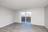 This single-floor unit is designed with a clean, neutral aesthetic throughout, featuring warm greige walls and white trim that create a cohesive, move-in-ready atmosphere. The open living area is finished with wood-style luxury vinyl plank flooring and is highlighted by a sliding glass patio door that fills the space with natural light and provides views of an outdoor patio and the surrounding neighborhood.

The kitchen is well-appointed with dark espresso cabinetry, granite-look countertops, a double basin sink, and black appliances including a refrigerator, dishwasher, and range. A window above the counter area brings in additional natural light. The layout connects efficiently to the main living and dining areas.

The bedrooms are carpeted for comfort and offer generous proportions. At least one bedroom features a spacious walk-in closet with dual shelving rods and built-in shelving, providing substantial storage capacity. Additional bedrooms include windows fitted with blinds for light control and privacy.

The bathroom is finished with wood-style tile flooring, a dark vanity with granite countertop, a large mirror, and a full tub-shower combination with a white surround. Brushed nickel fixtures and hardware complete the polished look throughout.