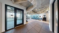 Power Up Gym is a modern fitness facility located at 757 Thomas St in Seattle, WA, offering a thoughtfully designed single-floor layout that accommodates a comprehensive range of workout activities. The space is divided into two primary zones, each serving a distinct fitness purpose.

The cardio and strength training area is lined with floor-to-ceiling windows that flood the room with natural light and frame views of the surrounding Seattle cityscape. This zone houses a row of treadmills, a stair climber, ellipticals, rowing machines, and a multi-station cable machine, alongside a full rack of kettlebells and dumbbells. Durable rubber flooring throughout provides both safety and comfort underfoot.

The second zone functions as an open, flexible workout space with large format tile flooring, wall-mounted mirrors, and a mounted display screen — ideal for group fitness, stretching, or functional training with stability balls and mats. Exposed ductwork and industrial-style ceilings give the gym a raw, urban aesthetic, while abundant glazing along the perimeter maintains a bright and energizing atmosphere. Glass-paneled doors connect the two areas, ensuring a cohesive and navigable layout. The overall design balances industrial character with a clean, functional environment suited for a wide variety of fitness routines.
