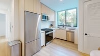 Located on Ohio Avenue in Westwood, Los Angeles, this thoughtfully designed 2-bedroom, 1-bathroom unit offers a clean, contemporary aesthetic throughout its efficiently utilized single floor. Light wood flooring flows seamlessly from room to room, creating a warm and cohesive feel against crisp white walls.

The primary bedroom stands out with striking wraparound floor-to-ceiling windows framed in matte black, flooding the space with natural light and offering leafy green views of the surrounding neighborhood. A second bedroom features its own large window and a wall-mounted mini-split system for individual climate control.

The kitchen is a functional highlight, outfitted with light wood cabinetry, white quartz countertops, a marble-effect tile backsplash, and a full suite of stainless steel appliances including a gas range, built-in microwave, dishwasher, and refrigerator. A window above the sink brings in natural light and outdoor views.

The bathroom is designed with a spa-inspired sensibility, featuring a frameless glass walk-in shower with textured white tile walls, a floating wood vanity with dual oval mirrors, matte black fixtures, and terrazzo-style flooring. The unit also includes dedicated laundry and two closets, maximizing storage within the compact layout.
