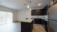 This single-floor residence showcases a thoughtfully designed open layout that seamlessly connects the kitchen and living areas. The kitchen is a standout feature, equipped with dark espresso shaker-style cabinetry reaching toward the ceiling for ample storage, granite countertops, and a full suite of stainless steel appliances including a dishwasher, range, over-the-range microwave, and refrigerator. A central island with matching granite provides additional prep space and casual seating, while two pendant lights with glass jar-style fixtures add a stylish focal point overhead. Wood-look plank flooring runs throughout the main living areas, contributing to a clean, contemporary aesthetic.

The bedrooms are carpeted for comfort and finished in neutral tones, with at least one room featuring a walk-in closet and a window that brings in natural light. The bathroom maintains the design consistency of the rest of the unit, featuring a dark vanity with granite countertop and a tub-shower combination with a sliding glass rod.

A dedicated in-unit laundry area with a stacked washer and dryer is tucked into its own closet space, adding functional convenience. Vertical blinds on a sliding glass door allow for privacy and light control. The overall ambiance is modern, clean, and move-in ready.