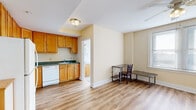 This efficiently designed one-bedroom, one-bathroom unit offers a well-organized layout across a single floor, making practical use of every square foot. Light wood laminate flooring flows consistently throughout all areas, lending a cohesive and clean aesthetic to the space.

The kitchen is a functional highlight, featuring warm honey-toned wood cabinetry arranged in an L-shape with ample upper and lower storage. It is equipped with a full suite of white appliances, including a refrigerator, electric range, dishwasher, and a double-basin sink with dark countertops. Flush ceiling lighting illuminates the workspace effectively.

Adjacent to the kitchen, the open living area provides enough room for a dining or work setup, with a window that invites natural light. The bedroom is a well-proportioned room featuring a ceiling fan with light fixture, a window with blinds for natural light and privacy, and neutral warm-toned walls. A second smaller room provides additional flexible space.

The bathroom features a full soaking tub with a tiled surround in classic white subway tiles, chrome fixtures, and a frosted window that allows natural light while maintaining privacy. Throughout the unit, white baseboards and neutral cream-toned walls create a bright, clean atmosphere suitable for a range of personal styles.