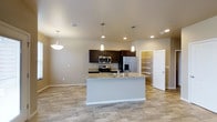 This two-story home showcases a well-designed open-concept main level centered around a functional kitchen. The kitchen features a large central island topped with light granite countertops, complete with a built-in sink and pendant lighting overhead. Dark espresso cabinetry lines the walls, providing ample storage, while stainless steel appliances — including a refrigerator with ice and water dispenser, microwave, and range — add a modern touch. Recessed lighting complements the pendant fixtures, keeping the space bright and welcoming. Adjacent to the kitchen, an open doorway leads to a walk-in pantry outfitted with built-in shelving, offering generous organizational storage. The kitchen flows seamlessly into the surrounding living and dining areas, enhanced by neutral-toned walls and light wood-look flooring that extends throughout the main level. The overall aesthetic is clean and contemporary, with a neutral color palette that creates a warm, move-in-ready atmosphere. The second floor likely provides additional living quarters, expanding the overall footprint of this thoughtfully designed home.
