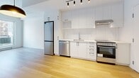 Located on the third floor at 4986 Place De La Savane in Montréal's Côte-des-Neiges–Notre-Dame-de-Grâce borough, this well-designed one-bedroom, one-bathroom unit offers a functional and modern living experience. The open-concept layout seamlessly connects the kitchen and living area, creating a bright and efficient use of space. Light hardwood flooring flows throughout, complementing the clean white walls and industrial-inspired exposed concrete ceiling and structural columns that lend the unit a contemporary loft-like character. The kitchen is outfitted with sleek white cabinetry featuring matte black hardware, white subway tile backsplash, light stone countertops, and a full suite of stainless steel appliances including a refrigerator, dishwasher, and range. A stylish pendant light and track lighting illuminate the space. The living area benefits from a large window that invites natural light and frames views of the surrounding neighbourhood. The bedroom is a cozy, private retreat featuring its own window with outdoor views and the same warm hardwood floors. The bathroom is finished with large-format beige floor tiles, a floating vanity with a mirrored medicine cabinet, and a glass-enclosed shower stall, all in a clean, neutral palette.