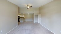 This executive 1-bedroom, 1-bathroom unit with a den offers a thoughtfully designed single-floor layout that maximizes both comfort and functionality. The open-concept living area is generously proportioned, featuring plush wall-to-wall carpeting in a neutral tone that complements the warm beige walls throughout. A ceiling fan with light fixture anchors the living space, providing both style and airflow. The kitchen is positioned adjacent to the main living area and features a raised bar-style counter that serves as a natural divider between the two spaces, ideal for casual dining or entertaining. White cabinetry and dark appliances give the kitchen a clean, classic look. A built-in closet with double doors is conveniently located within the living area, offering ample built-in storage. The den provides additional flexible space that can serve as a home office, guest room, or secondary lounge area. The unit benefits from vaulted or elevated ceiling lines that contribute to an airy, open ambiance throughout. Neutral finishes, clean lines, and an efficient floor plan make this an adaptable and comfortable executive living space suited to a variety of lifestyles.