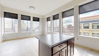 Located at 730 Hennepin Ave in the heart of Minneapolis, this two-bedroom, two-bathroom residence offers a thoughtfully designed single-floor layout. Distinctive terrazzo flooring flows consistently throughout the entire space, lending a polished, cohesive aesthetic to every room.

The kitchen is a standout feature, showcasing rich dark-wood cabinetry reaching toward the ceiling, gray stone-toned countertops, black appliances including a range, dishwasher, refrigerator, and microwave, along with a central island that provides additional prep and storage space. Large windows surrounding the kitchen area frame impressive panoramic views of the Minneapolis downtown skyline, filling the space with natural light.

Both bedrooms are well-proportioned and include built-in closets with wire shelving systems, offering practical storage solutions. Light wood trim and doors provide a clean, modern contrast throughout. The hallway connects the rooms efficiently, featuring a ceiling light fixture and a thermostat for climate control.

Each of the two bathrooms is finished with rich dark-wood vanities, white countertops, full bathtub and shower combinations, and coordinating terrazzo flooring, maintaining the consistent design language of the residence. The overall ambiance is clean, urban, and functional, well-suited for city living in a prime Minneapolis location.