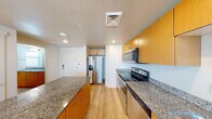This single-floor residence offers a clean, modern aesthetic carried consistently throughout its thoughtfully designed layout. The kitchen serves as a central highlight, showcasing warm honey-toned cabinetry paired with speckled granite countertops and a full suite of stainless steel appliances, including a French door refrigerator with ice and water dispenser, an electric range with over-the-range microwave, and a dishwasher. A generous kitchen island provides additional prep and dining space, while light hardwood flooring extends seamlessly through the main living areas, adding warmth and continuity.

The bathroom continues the granite theme with a wide dual-sink vanity topped in blue-toned speckled stone and framed by a large wall mirror with contemporary vanity lighting. Multiple windows with horizontal blinds allow natural light to fill the space while maintaining privacy. The bedroom is bright and airy, benefiting from multiple windows, a ceiling fan, and the same light hardwood flooring, creating a comfortable and well-ventilated retreat.

A dedicated laundry area features a stacked washer and dryer unit alongside built-in hanging rods, offering practical in-unit convenience. Recessed lighting and a textured ceiling complete the polished, functional character of this residence.