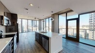 Located in the heart of Downtown Los Angeles, this high-rise unit at 801 S Hope St offers a striking blend of industrial and contemporary design. Expansive floor-to-ceiling windows wrap around the living areas, flooding the space with natural light and framing dramatic panoramic views of the Los Angeles skyline and surrounding cityscape. Exposed concrete columns, ceilings, and accent walls lend an urban, loft-inspired character throughout, complemented by wide-plank hardwood flooring that runs seamlessly across the open layout. The kitchen is a standout feature, showcasing a large center island with a white quartz countertop and undermount sink, dark espresso cabinetry, stainless steel appliances including a range, microwave, and refrigerator, and a sleek tile backsplash. Pendant lighting and a ceiling fan add functional style to the open living and dining area. The bedrooms offer generous proportions, with corner windows maximizing views and natural light. Bathrooms are finished with clean, modern tilework, including a glass-enclosed shower and a separate tub-and-shower combination. A walk-in closet with built-in shelving provides ample storage. The overall ambiance is polished and urban, ideal for experiencing the energy of Downtown Los Angeles.
