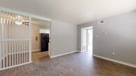 This single-story unit offers a practical and cohesive layout designed for comfortable everyday living. The living area is finished with durable wood-style flooring and neutral gray walls, creating a clean, understated aesthetic. A textured ceiling adds dimension overhead, while a wall-mounted thermostat and multiple electrical outlets reflect thoughtful functionality. A decorative slatted partition element adds a subtle architectural detail near the entryway.

The galley-style kitchen runs along two parallel walls, providing ample cabinetry in white with coordinating light countertops. Black appliances — including a refrigerator, electric range, and dishwasher — offer a bold contrast to the white cabinetry. Light-toned flooring and a ventilation hood complete the kitchen's efficient design.

The bedroom is carpeted for warmth and comfort, featuring a ceiling fan with a light fixture, a window that allows natural light to filter in, and a textured ceiling consistent with the rest of the unit. The full bathroom includes a white vanity with granite-style countertops, a large mirror, a tub-shower combination, and wood-style flooring, maintaining the unit's cohesive design language throughout.