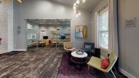 Located at 9500 Brightway Ct in Henrico, Virginia, this dynamic single-floor commercial space offers a thoughtfully designed environment that balances productivity with comfort. The interior is defined by a bold, contemporary aesthetic, with striking teal accent walls, layered stone-look tile detailing, and rich mixed flooring that transitions between warm hardwood and textured carpet.

The open-plan main area provides generous room for collaborative workstations and flexible seating arrangements, bathed in natural light from multiple windows dressed with clean, neutral curtains. A welcoming lounge zone anchors the space with a wall-mounted electric fireplace set against a textured stone feature wall, a vivid blue area rug, and a vibrant pink accent chair with ottoman — all beneath a sculptural sputnik chandelier.

A dedicated reception and seating area near the glass-front entrance features a round marble-top table with bold red swivel chairs, framed by large windows overlooking the exterior. Adjacent, a sophisticated lounge with glass-panel sliding doors reveals private office spaces fitted with built-in cabinetry and workstations.

The fully equipped kitchen/break room showcases modern grey cabinetry, white upper cabinets, a textured stone backsplash, light countertops, a utility sink, and bar-height seating — an ideal space for daily use. Throughout, curated artwork and eclectic furnishings contribute to a creative, professional atmosphere.