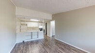 This 1-bedroom, 1-bathroom unit offers a practical and well-designed single-floor layout. Rich wood-look flooring flows consistently throughout the entire space, complemented by neutral taupe walls and crisp white trim, creating a clean and cohesive aesthetic.

The open-concept living area connects seamlessly to the kitchen via a half-wall divider with built-in shelving, allowing natural light from the front window to reach both spaces. The kitchen is outfitted with white shaker-style cabinetry, granite-look countertops, a stainless steel single-basin sink, and a stainless electric range with an overhead ventilation hood, providing ample functionality for everyday cooking.

The living area features a textured ceiling and a large window that brings in natural light, along with direct access to the front entry door. The bedroom is a comfortable, well-proportioned room with its own window fitted with blinds, a ceiling fan with light fixture, and the same warm wood-look flooring.

The full bathroom includes a white vanity with storage, a toilet, and a shower-tub combination with a clean white surround. Throughout the unit, white panel doors and consistent finishes contribute to a tidy, move-in-ready presentation. The textured ceilings appear in all rooms, adding a subtle design element that ties the space together.