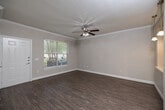 This single-floor residence offers a thoughtfully designed layout with a cohesive, neutral color palette throughout. The open-concept living area features rich hardwood-style flooring and elegant crown molding, creating a polished and inviting atmosphere. A ceiling fan provides comfort, while a large window allows natural light to fill the space with a bright, airy feel. The living area connects seamlessly to the kitchen via a stylish arched passageway, adding a distinctive architectural touch. The kitchen is well-equipped with dark espresso cabinetry, black appliances including a refrigerator, range, and built-in microwave, complemented by track lighting and a peninsula that serves as both a workspace and casual dining area. The bedrooms are finished with plush carpeting, ceiling fans, and windows with blinds that allow for adjustable natural light. A full bathroom features dark wood vanity cabinetry, a tiled tub-shower combination with a decorative accent tile border, and hardwood-style flooring. A dedicated laundry closet houses a full-size washer and dryer, adding everyday convenience. White panel doors and clean baseboards throughout contribute to the home's neat, cohesive aesthetic.