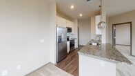 Located at 22415 Market St. in Cornelius, NC, this single-floor residence offers a thoughtfully designed layout with modern finishes throughout. The open-concept kitchen is a standout feature, showcasing granite countertops on a generous peninsula with an undermount sink, white shaker-style cabinetry, a classic subway tile backsplash, and a full suite of stainless steel appliances including a side-by-side refrigerator, electric range, and microwave. Stylish pendant lighting adds a contemporary touch above the kitchen peninsula, which flows seamlessly into the adjacent carpeted living area. The bedrooms are well-proportioned, each featuring plush carpet flooring, ceiling fans, and bright windows that invite natural light and offer views of the surrounding neighborhood. Multiple bedrooms include walk-in closets outfitted with wire shelving systems for organized storage. The bathrooms are finished with granite countertops and white cabinetry; the primary bathroom features a dual-sink vanity with a large mirror and access directly to the walk-in closet. A secondary bathroom offers a single-sink vanity with matching granite finishes and wood-look flooring. Neutral warm tones and clean lines create a cohesive, welcoming ambiance throughout the entire space.