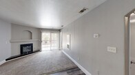 This single-floor, one-bedroom, one-bathroom unit offers a well-organized layout across a compact yet functional footprint. The living room serves as the heart of the space, featuring a corner fireplace with a classic white mantel, a built-in arched display niche, and a sliding glass door with vertical blinds that allows natural light to filter in and provides outdoor views. The living area transitions seamlessly between plush wall-to-wall carpeting and dark hardwood-style flooring, with a ceiling fan adding both style and practicality. The kitchen is equipped with rich dark-brown cabinetry, light quartz countertops, a double stainless steel sink with a pull-down faucet, and stainless steel appliances, creating a clean and modern workspace. The bathroom features wood-look flooring, a dark-stained vanity with a vessel sink, a large mirror with a multi-bulb vanity light fixture, and a full soaking tub with a shower, offering a spa-like feel. The bedroom is a quiet retreat with soft carpeting, neutral gray walls, and a window fitted with blinds that brings in natural light while maintaining privacy. Throughout the unit, a cohesive neutral color palette, white baseboards, and consistent finishes provide a clean, modern aesthetic.