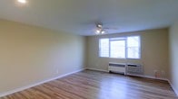 Located at 118 Montgomery Avenue in Bala Cynwyd, Pennsylvania, this single-floor residence offers a clean, well-maintained living environment with classic design details throughout. The main living area is finished with warm hardwood flooring that extends across the room, contributing to a bright and inviting atmosphere. A ceiling fan with integrated lighting is centrally positioned, providing both air circulation and ambient illumination. Large windows along the exterior wall allow generous natural light to fill the space, offering views of the surrounding neighborhood. A baseboard heating unit and wall-mounted air conditioning unit are present beneath the windows, ensuring year-round climate comfort. The walls are finished in a neutral, light tone that complements the natural wood floors and enhances the overall sense of openness. White baseboards and trim provide clean architectural definition throughout the room. The layout is open and functional, offering flexible possibilities for furnishing and use. The space reflects a straightforward, practical design that prioritizes comfort and livability, making it well-suited for a variety of occupants. Situated in the desirable Bala Cynwyd community of Lower Merion Township, the property benefits from a convenient suburban location with easy access to local amenities.