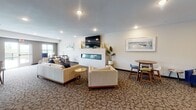 Located at 540 Tyler Rd S in Red Wing, Minnesota, this single-floor community common space is thoughtfully designed to encourage social interaction and comfortable everyday living. The layout flows seamlessly across distinct functional zones, all unified by patterned carpeting, recessed lighting, and a warm, contemporary aesthetic.

The fully equipped communal kitchen serves as a central hub, featuring rich dark cabinetry, granite countertops, stainless steel appliances including a refrigerator, range, microwave, and dishwasher, and a generous island with bar-height seating. Pendant lighting above the island adds a refined touch, while light wood-look tile flooring grounds the space practically and stylishly.

Adjacent to the kitchen, a coffee station with a single-serve brewer and dark wood credenza provides a convenient spot for daily refreshment. Decorative gold ginkgo leaf wall art adds an artistic accent to this transitional area.

The lounge area is expansive and inviting, anchored by a sleek linear fireplace framed in white tile with a wall-mounted television above. Comfortable neutral sofas and accent chairs are arranged for both intimate conversation and open gathering. Multiple dining and café-style seating clusters are positioned near large windows, filling the space with natural light and offering views of the surrounding landscape. The overall ambiance is modern, relaxed, and well-suited for community life.